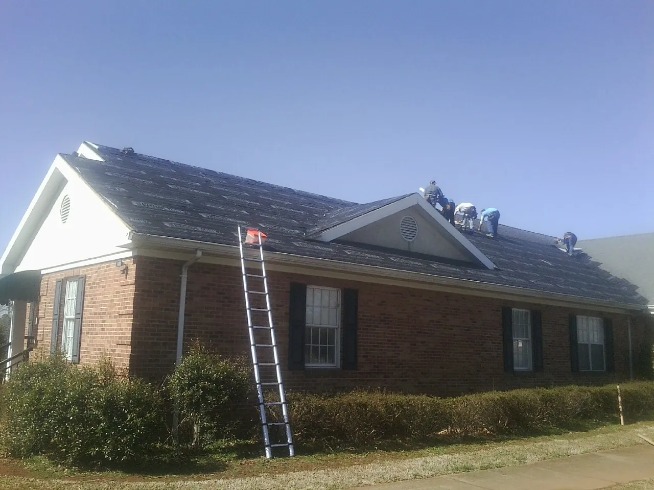 Crew tearing shingles off a brick ranch roof with a ladder set — Metal Roof Repair work by our crew in Harsens Island