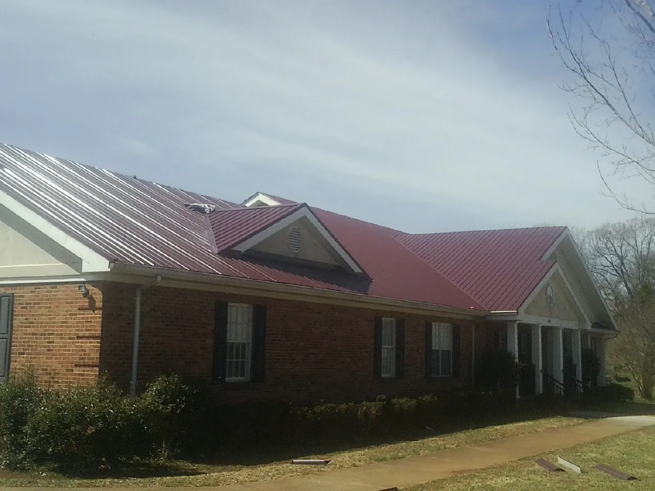 Red metal roof with gabled entries on a long brick building, from a Hail Damage Roof Repair job in Harsens Island