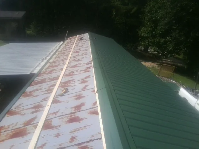 Old rusted panels beside newly installed green metal roofing — Wind Damage Roof Repair by Roofing Brothers in Harsens Island