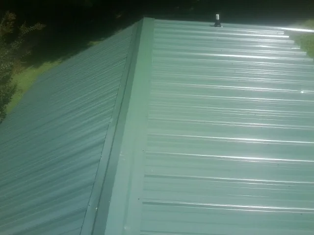 New green metal panels meeting at the ridge of a roof — Flat Roof Repair work by our crew in Harsens Island