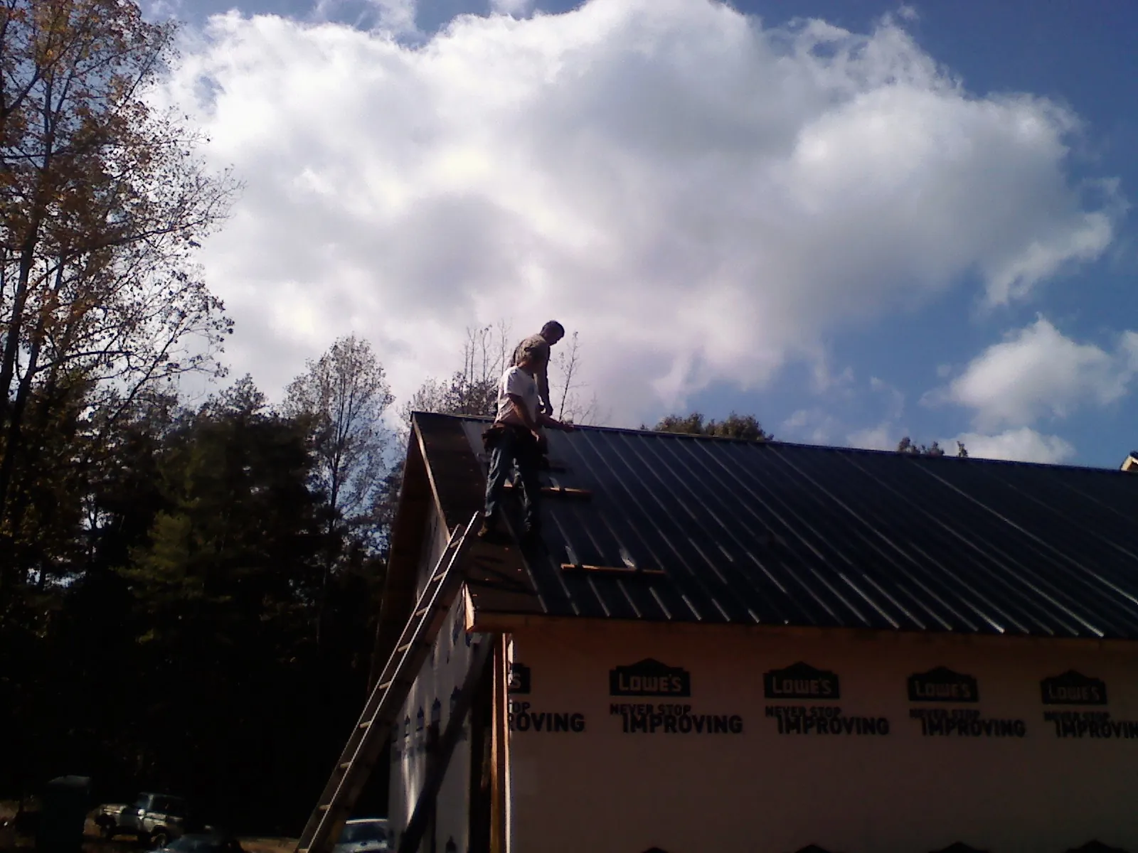 Roofer fastening dark metal panels high against a cloudy sky, from a Roof Inspection job in Harsens Island