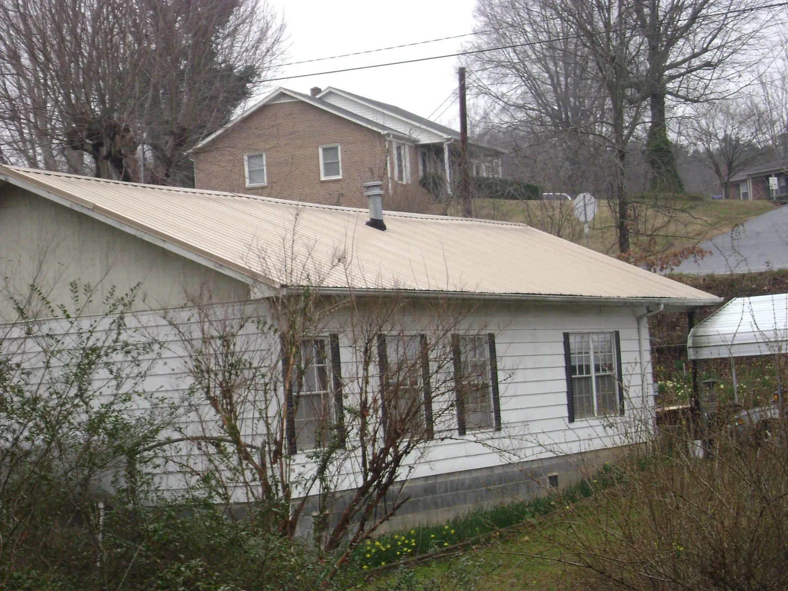 Tan metal roof on a white sided house set into a hillside — Commercial Roofing by Roofing Brothers in Harsens Island