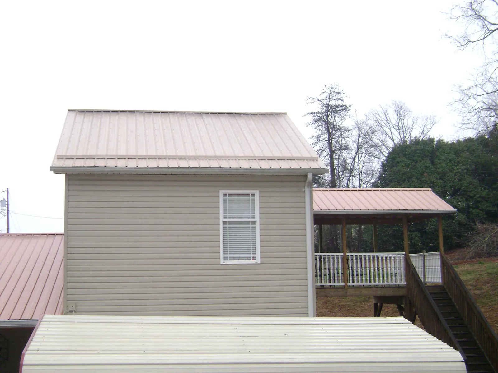 Tan metal roofs on a two story addition and attached porch, from a Roof Replacement job in Harsens Island